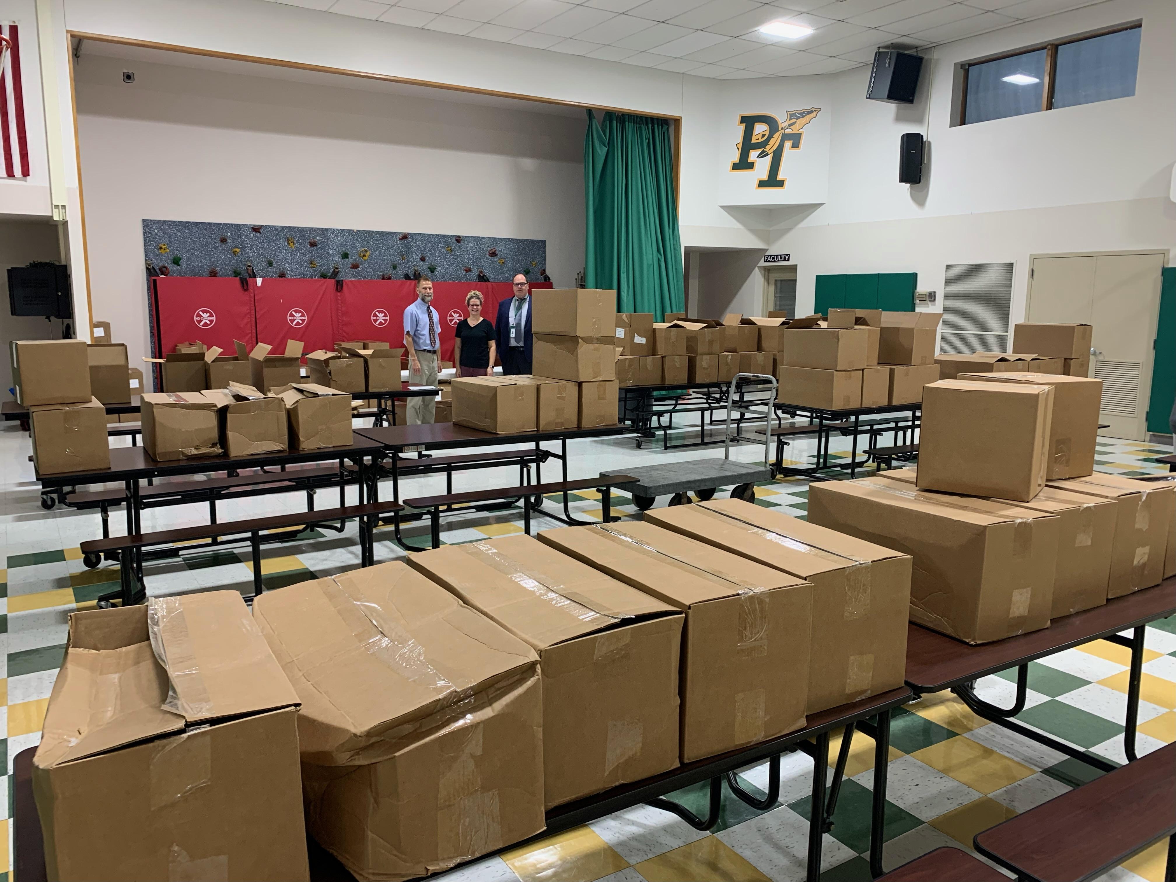 Principal Mr. Marasti, Library Aide Sarah Schadler, and Superintendent Dr. Harris stand amidst the cases of books earned by McCullough students